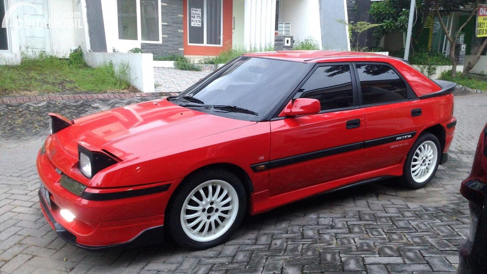 Gambar sebuah mobil Mazda Astina berwarna merah dilihat dari sisi depan